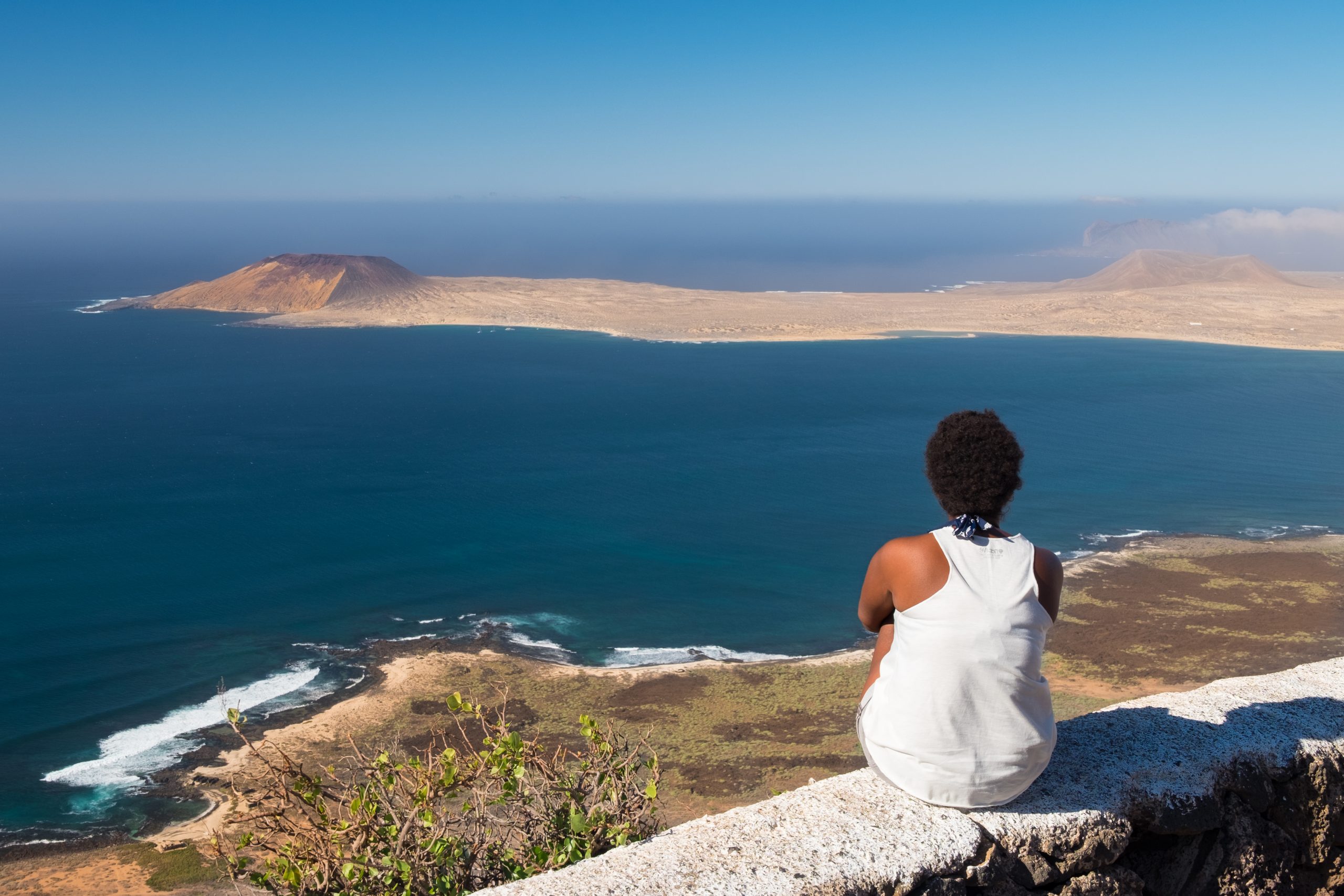 rear-view-woman-sitting-stone-wall-against-sea